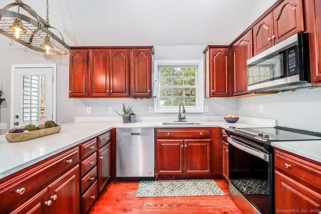 kitchen featuring light wood finished floors, a sink, reddish brown cabinets, and appliances with stainless steel finishes