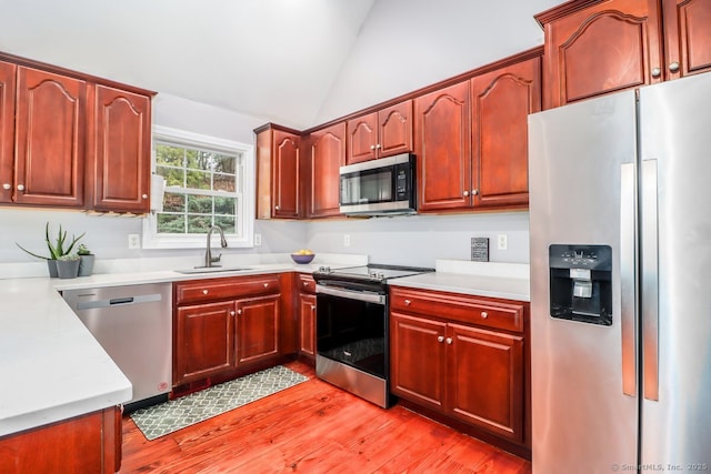 kitchen with light wood-style flooring, a sink, light countertops, lofted ceiling, and stainless steel appliances