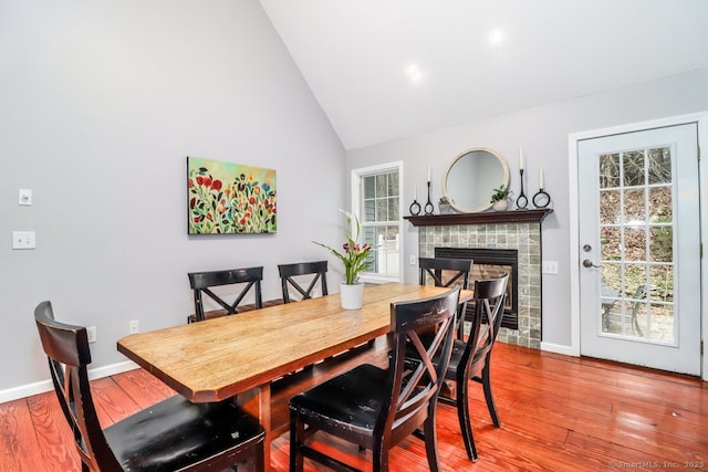 dining space featuring wood finished floors, high vaulted ceiling, a fireplace, and baseboards