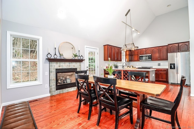 dining room featuring high vaulted ceiling, visible vents, a tiled fireplace, light wood finished floors, and baseboards