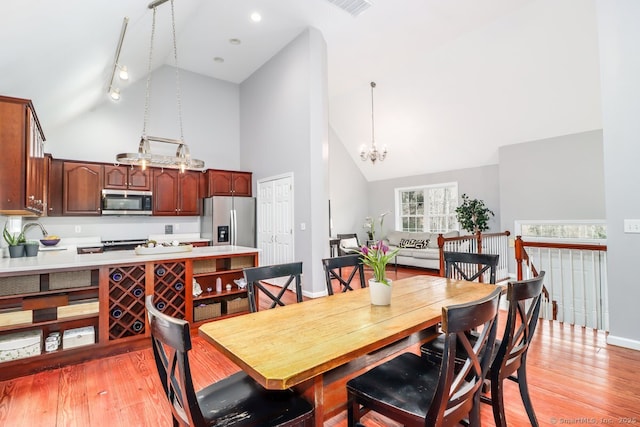dining room with high vaulted ceiling, light wood-style flooring, and a chandelier