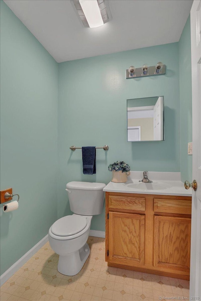 half bath with toilet, baseboards, vanity, and tile patterned floors