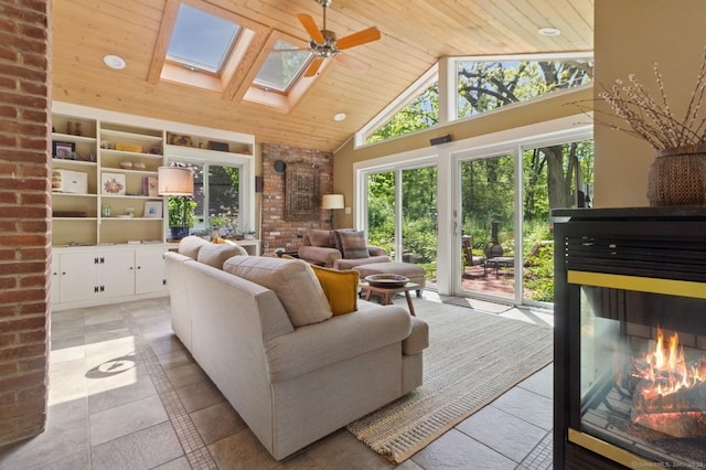 living area with wood ceiling, high vaulted ceiling, a glass covered fireplace, a skylight, and a ceiling fan
