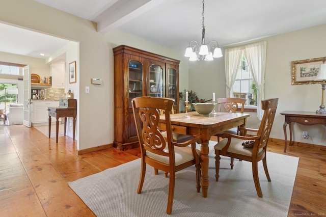 dining space featuring healthy amount of natural light, a chandelier, light wood finished floors, baseboards, and beam ceiling