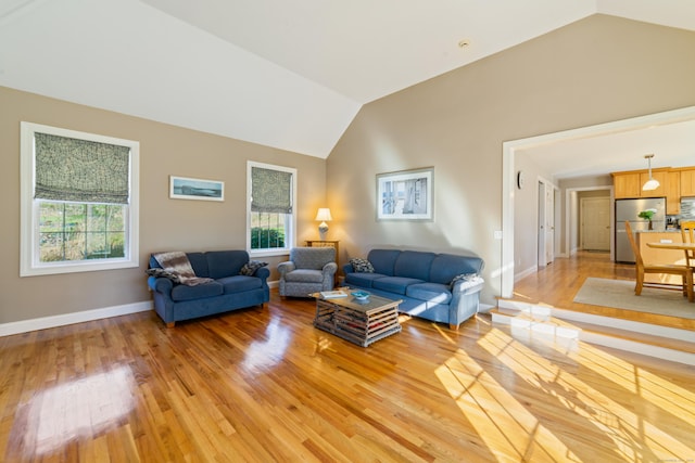 living area with baseboards, vaulted ceiling, light wood finished floors, and plenty of natural light