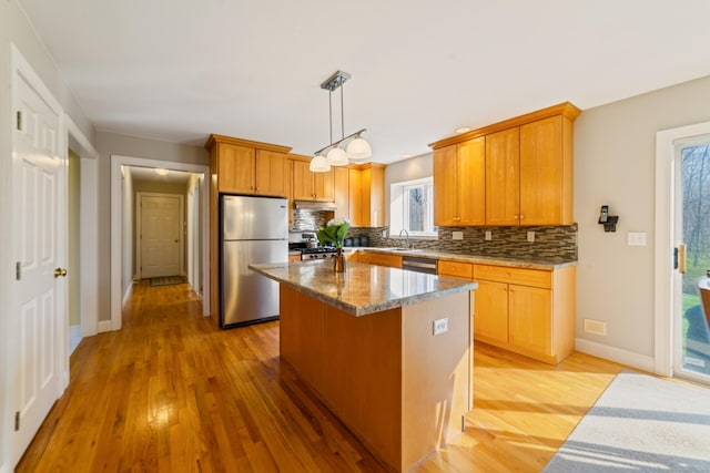 kitchen featuring stainless steel appliances, a sink, tasteful backsplash, baseboards, and light wood-style floors