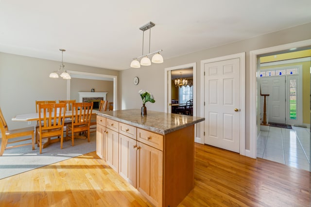 kitchen featuring a center island, light wood-type flooring, a chandelier, stone countertops, and a fireplace