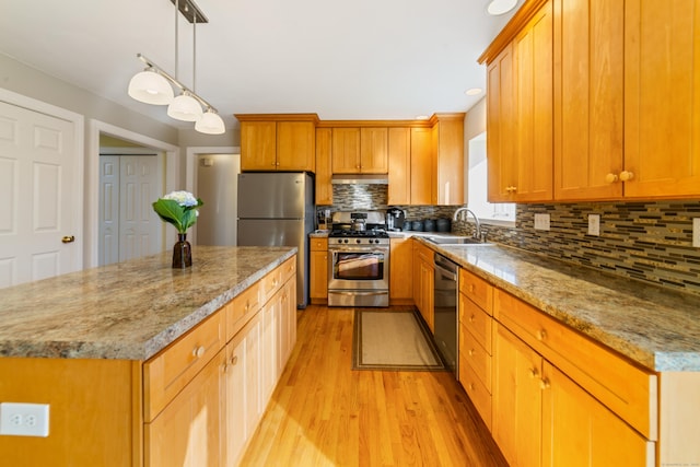 kitchen with light wood finished floors, a sink, decorative backsplash, a kitchen island, and appliances with stainless steel finishes