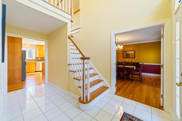 stairs with a towering ceiling, tile patterned floors, baseboards, and an inviting chandelier