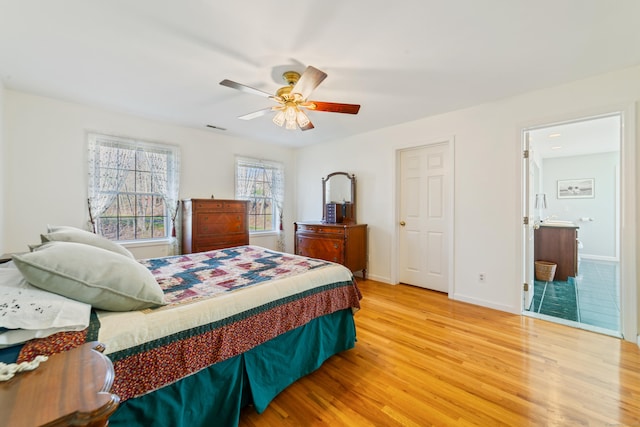bedroom featuring light wood finished floors, visible vents, a ceiling fan, baseboards, and ensuite bathroom
