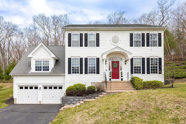 colonial home with an attached garage, aphalt driveway, and a front yard