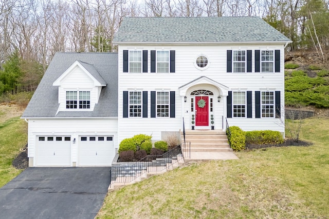colonial-style house with a front lawn, driveway, roof with shingles, and a garage