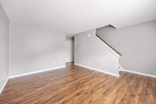 unfurnished living room featuring wood finished floors, baseboards, and stairway