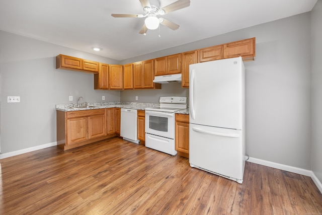 kitchen featuring under cabinet range hood, baseboards, white appliances, and a sink