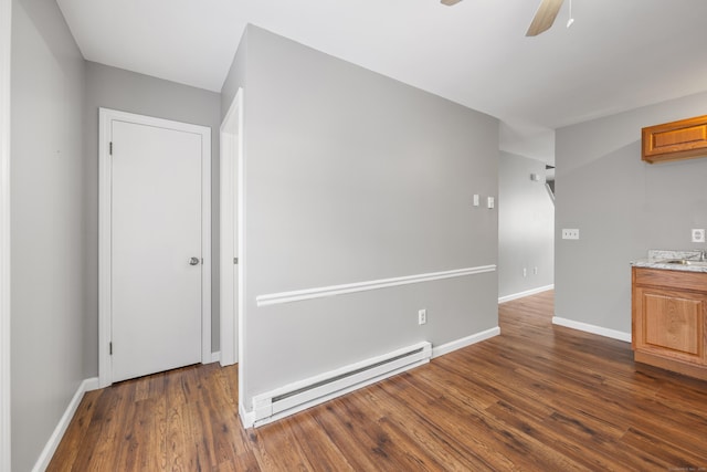 unfurnished room featuring a baseboard heating unit, a sink, baseboards, a ceiling fan, and dark wood-type flooring