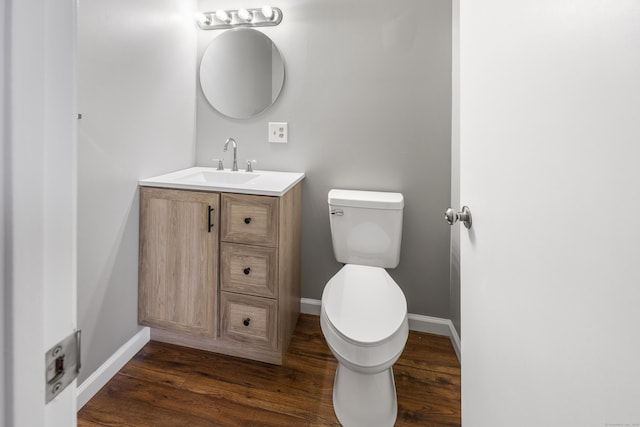 half bathroom with wood finished floors, baseboards, vanity, and toilet