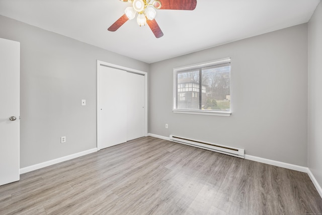 unfurnished bedroom featuring wood finished floors, a baseboard heating unit, a closet, baseboards, and ceiling fan