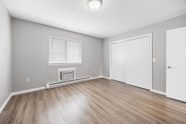 unfurnished bedroom featuring a baseboard heating unit, baseboards, wood finished floors, and a closet