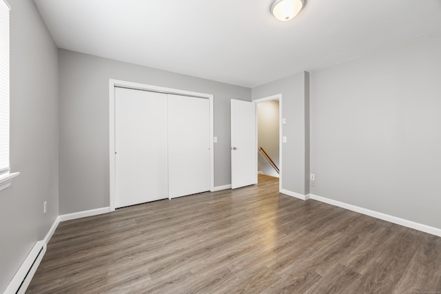 unfurnished bedroom featuring baseboard heating, baseboards, wood finished floors, and a closet