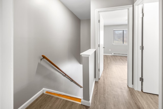 hall featuring light wood-type flooring, baseboard heating, and an upstairs landing