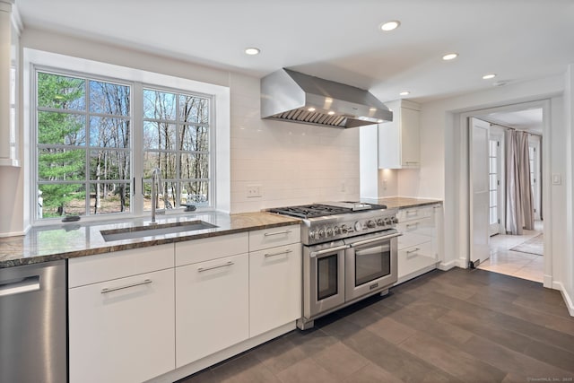 kitchen with a sink, stone countertops, backsplash, wall chimney exhaust hood, and appliances with stainless steel finishes