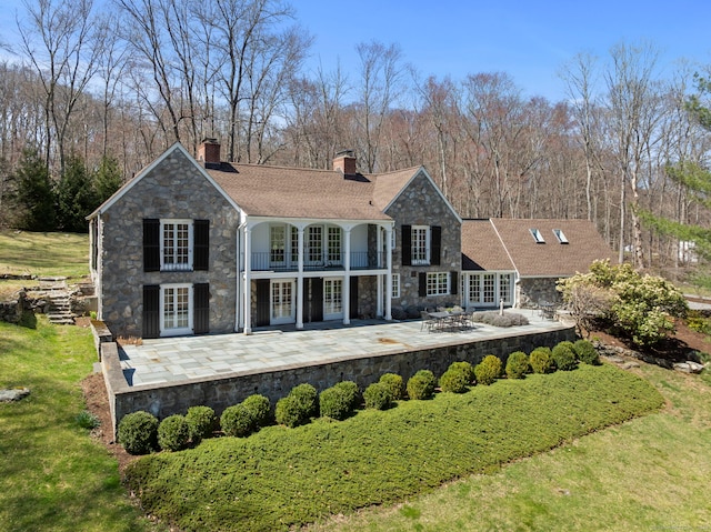 rear view of property with stone siding, a patio area, french doors, and a balcony
