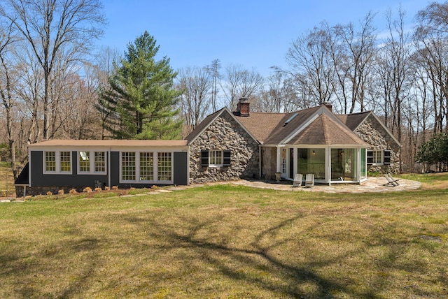 rear view of property featuring a patio area, a chimney, a yard, and stone siding