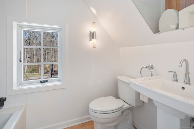 bathroom with a bathtub, a sink, toilet, vaulted ceiling, and baseboards