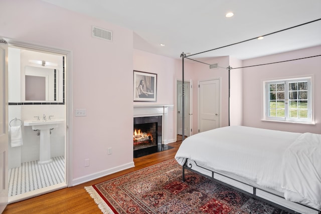 bedroom featuring a fireplace with flush hearth, wood finished floors, and visible vents