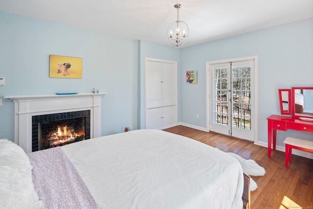 bedroom featuring an inviting chandelier, baseboards, wood finished floors, and a warm lit fireplace