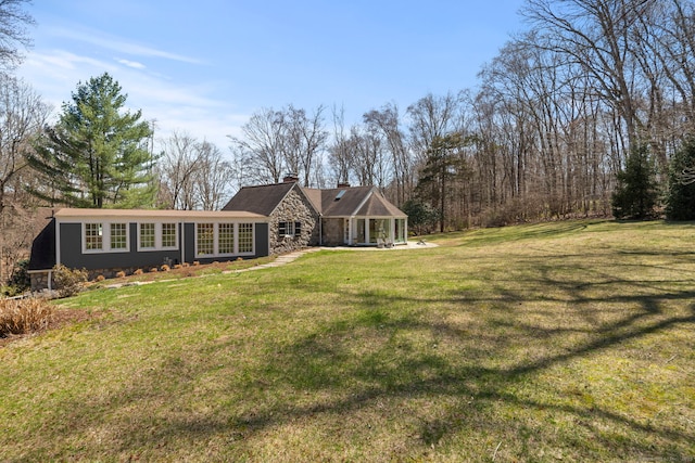 view of front of property featuring a front yard, stone siding, and a chimney