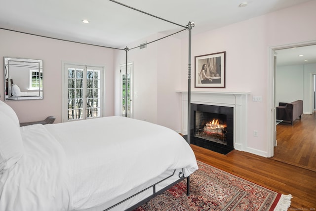 bedroom with a fireplace with flush hearth, baseboards, wood finished floors, and recessed lighting