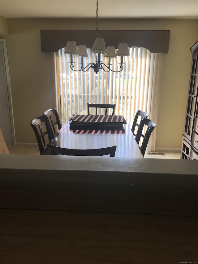 carpeted dining space with a chandelier and baseboards