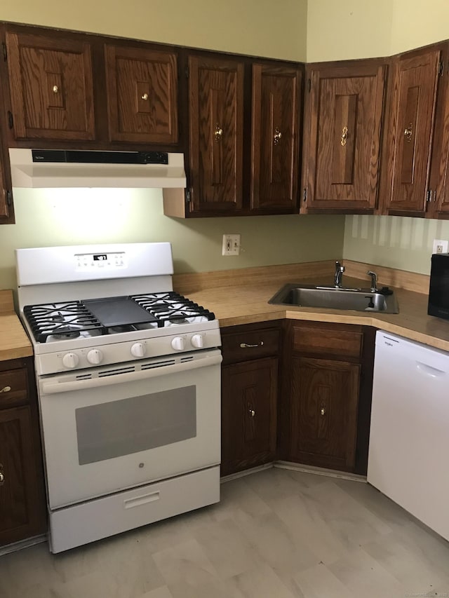 kitchen with dark brown cabinetry, white appliances, light countertops, under cabinet range hood, and a sink