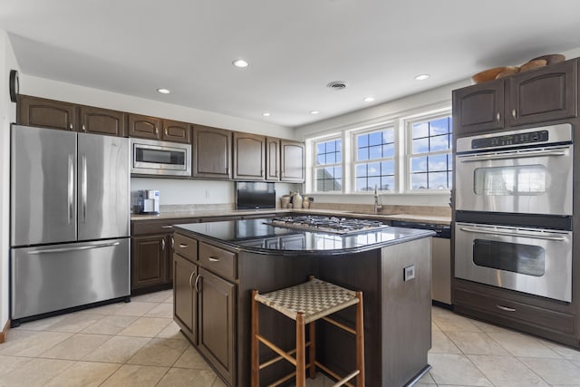 15 Buckingham Ave, Old Saybrook, CT 06475 - kitchen with appliances with stainless steel finishes, light tile patterned floors, a center island, dark brown cabinetry, and a breakfast bar