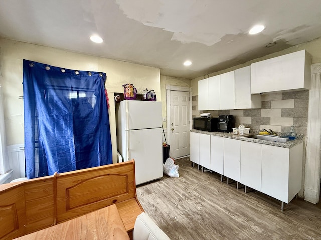 kitchen with freestanding refrigerator, black microwave, white cabinets, wood finished floors, and a sink