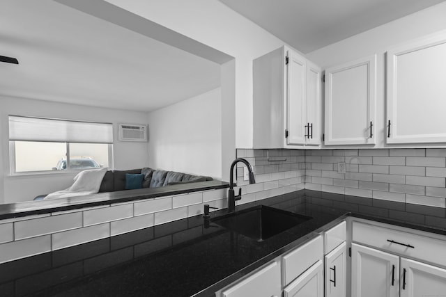 136 Pembroke Rd Unit 6-49, Danbury, CT 06811 - kitchen with dark countertops, a wall mounted air conditioner, white cabinets, a sink, and backsplash
