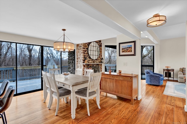 dining room featuring a chandelier, plenty of natural light, light wood finished floors, and a stone fireplace