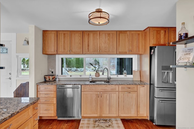 kitchen with wood finished floors, dark stone counters, stainless steel appliances, and a sink