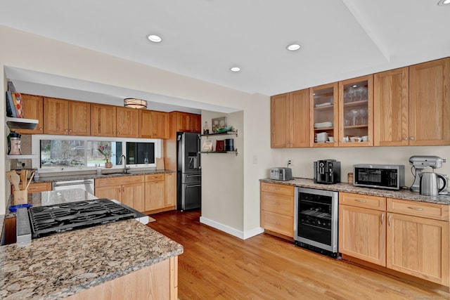 kitchen with wine cooler, light wood-style floors, light stone countertops, glass insert cabinets, and appliances with stainless steel finishes