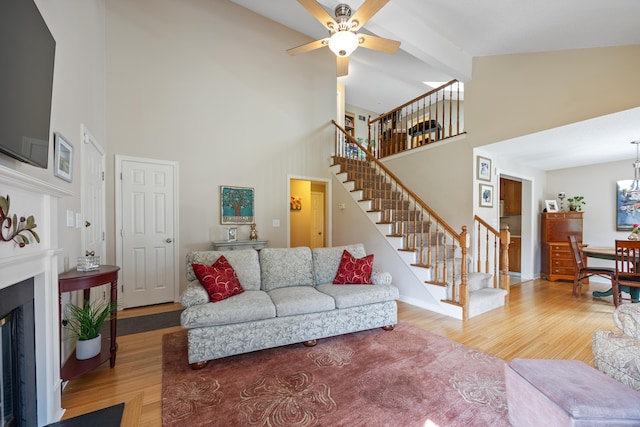 living area with light wood finished floors, ceiling fan, high vaulted ceiling, and stairway