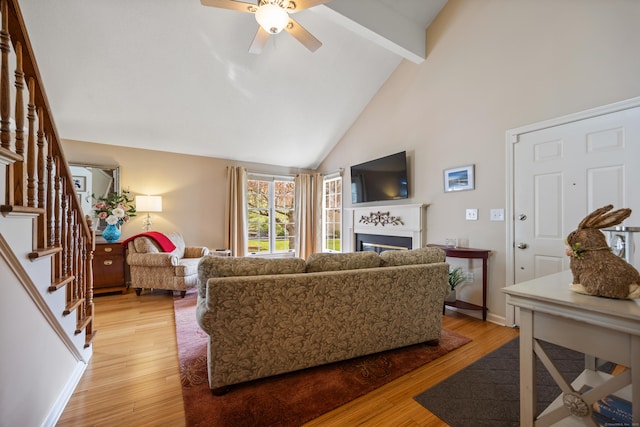 living room with a ceiling fan, beamed ceiling, light wood-style flooring, and a fireplace