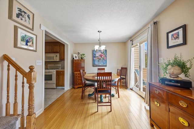dining area with stairs, a textured ceiling, an inviting chandelier, and light wood-style floors