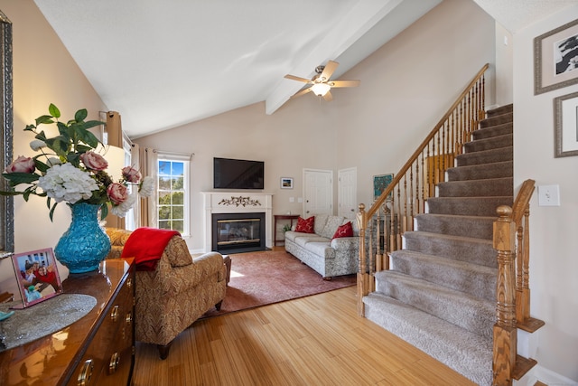 living room featuring stairs, a ceiling fan, a fireplace with flush hearth, wood finished floors, and beamed ceiling