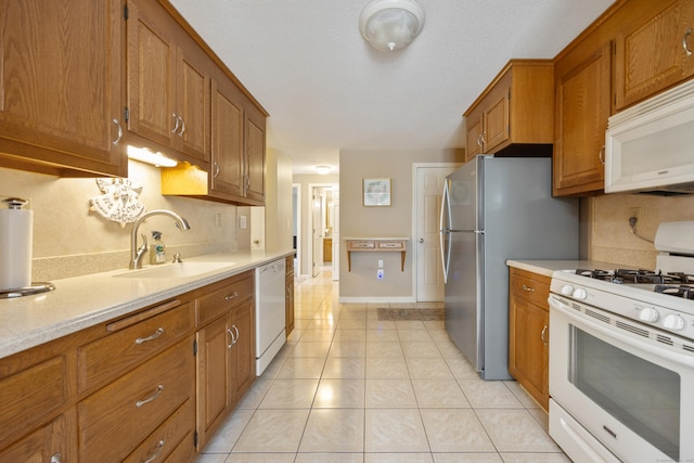 kitchen featuring a sink, white appliances, light countertops, brown cabinetry, and light tile patterned floors