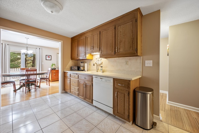 kitchen featuring light countertops, white dishwasher, brown cabinets, and a notable chandelier