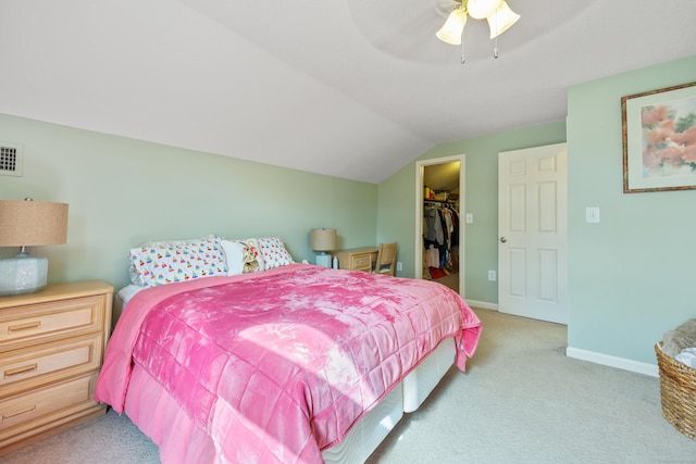 bedroom with a closet, baseboards, a walk in closet, light colored carpet, and vaulted ceiling