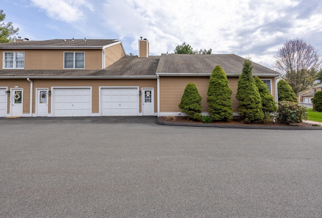 view of front of property featuring a garage, a shingled roof, a chimney, and driveway