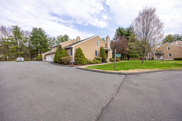 view of property exterior with an attached garage, driveway, a yard, and a chimney
