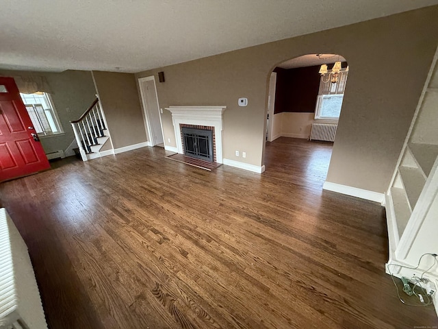 unfurnished living room with radiator heating unit, wood finished floors, arched walkways, and stairs